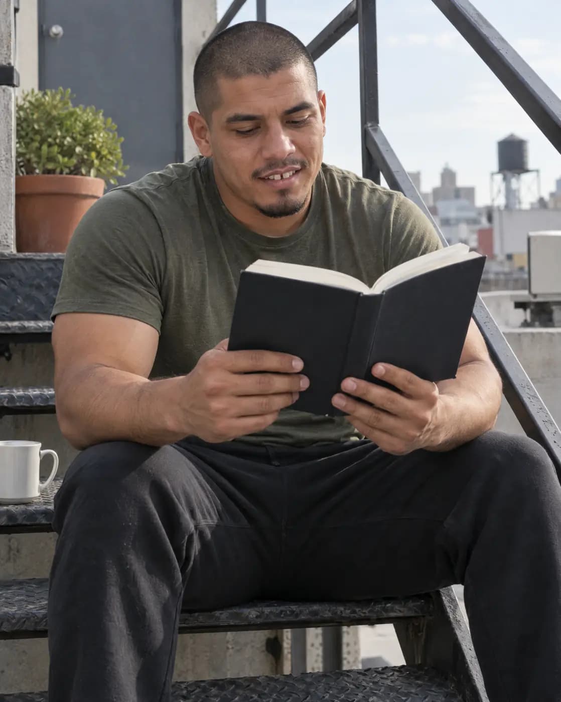A Latino man, 31, muscular, buzzed hair, light beard patch, gap teeth reads on a rooftop stair