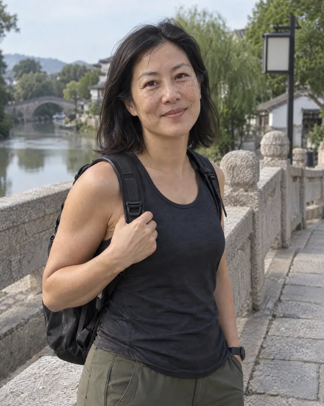 An East Asian woman, 44, athletic, shoulder-length black hair, sun spots pauses on a stone bridge path